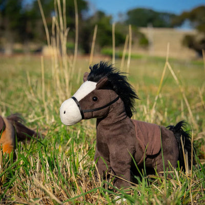 Plush horse toy in a grassy field with trees in the background